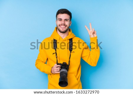 Young caucasian photographer man isolated joyful and carefree showing a peace symbol with fingers.