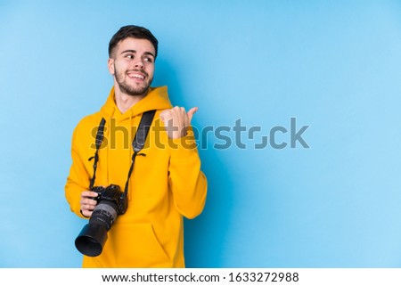 Young caucasian photographer man isolated points with thumb finger away, laughing and carefree.