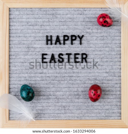 The words Happy Easter on grey felt letter board decorated with quail eggs and feathers