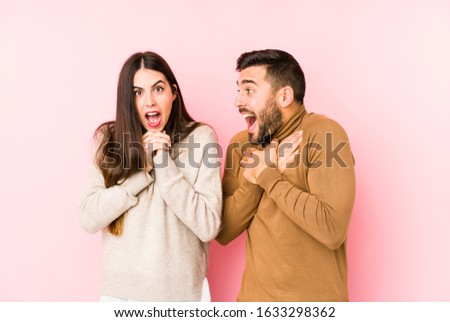 Young caucasian couple isolated praying for luck, amazed and opening mouth looking to front.