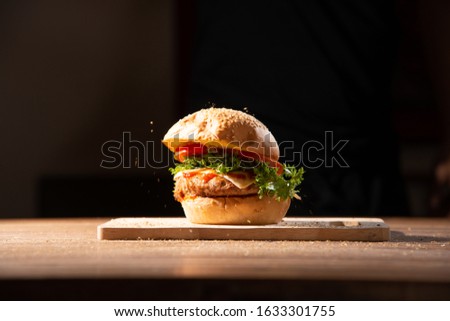 home made hamburger made by white sesame bun, tomato slice, salad, cheese, grilled meat and onion on wooden tray wooden table with dark isolate background stock photo