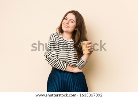 Young curvy woman holding a coffee laughing and having fun.