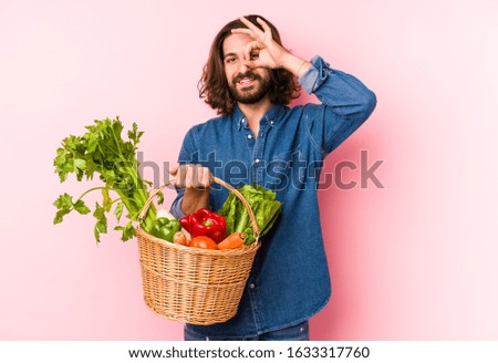 Young man picking organic vegetables from his garden isolated excited keeping ok gesture on eye.