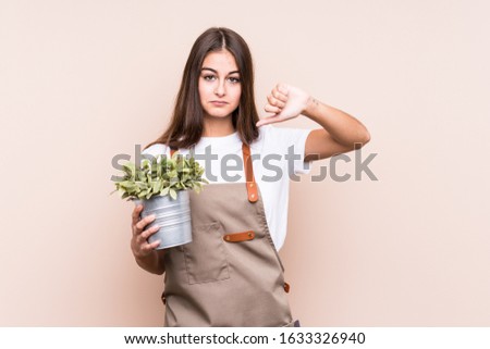 Young gardener caucasian woman holding a plant isolatedshowing a dislike gesture, thumbs down. Disagreement concept.