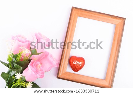 Top view of artificial pink roses with text LOVE on heart shape and wooden frame on white background. Love and Valentine's Day concept. Selective focus.