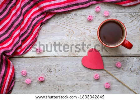 Simple and cute romantic picture with a cup of tea, pink striped scarf and red heart on a wooden background for Valentine's day