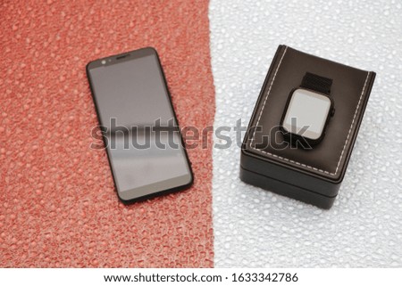 Smartphone and smartwatch in a black gift box on a blue-green background in the form of water drops.