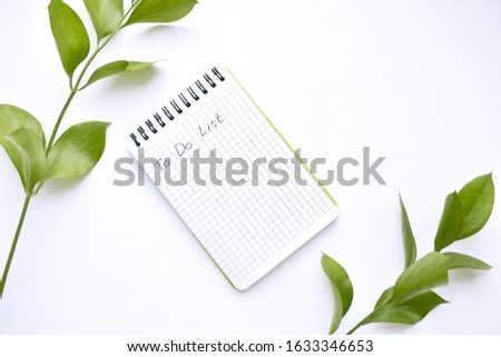 White spiral notebook and green leaves on a white background. Top view. Copy space.