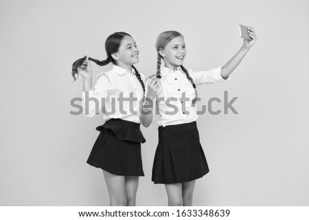 One more selfie. Happy schoolchildren taking selfie with smartphone on yellow background. Little girls smiling to selfie camera in mobile phone. Enjoying selfie session on september 1.