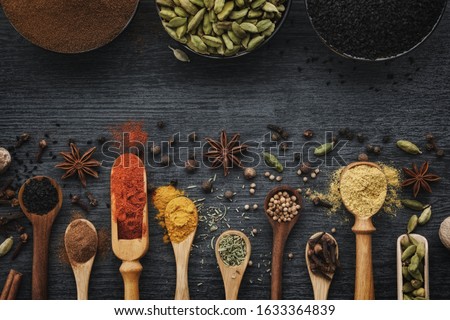 Various aromatic colorful spices and herbs in wooden spoons and scoops. Black ceramic bowls of seasonings. Ingredients for cooking.  Ayurveda treatments. Top view. Royalty-Free Stock Photo #1633364839