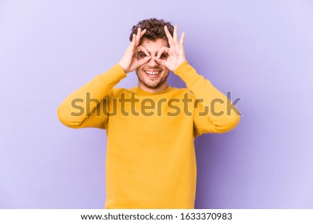 Young blond curly hair caucasian man isolated showing okay sign over eyes