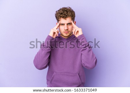Young blond curly hair caucasian man isolated focused on a task, keeping forefingers pointing head.