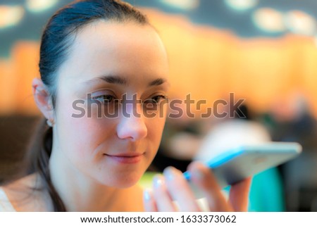 Woman talking on a mobile phone , voice recognition. Happy girl using the voice recognition of the phone sitting in a trendy cosy coffee shop cafe. toned
