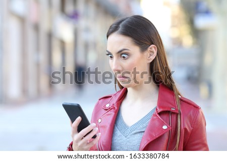 Perplexed woman checking smart phone news standing in the street Royalty-Free Stock Photo #1633380784