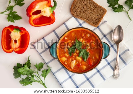 Hungarian goulash in a ceramic plate, bread, paprika, parsley on a white table, top view. Healthy food rich in vitamins, antioxidants and fiber. Royalty-Free Stock Photo #1633385512