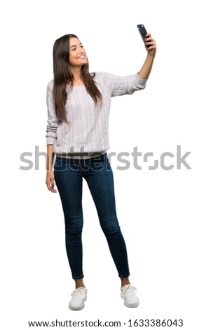 A full-length shot of a Young hispanic brunette woman making a selfie over isolated white background