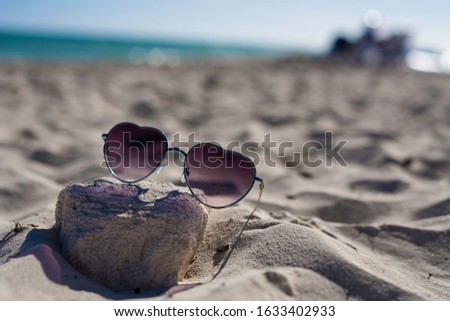 Heart Shape Cool Sunglasses in the sand on a tropical white sand beach. Vacation sunglasses.