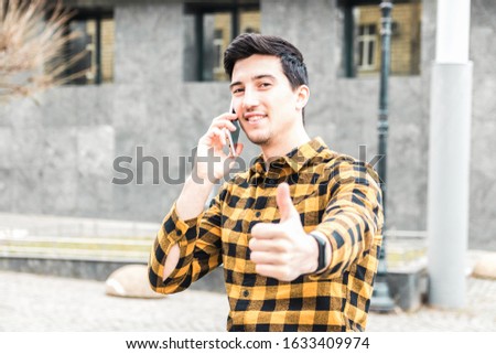 university enrollment. handsome young man or student with smile on face speaking on the phone and showing big thumb up.