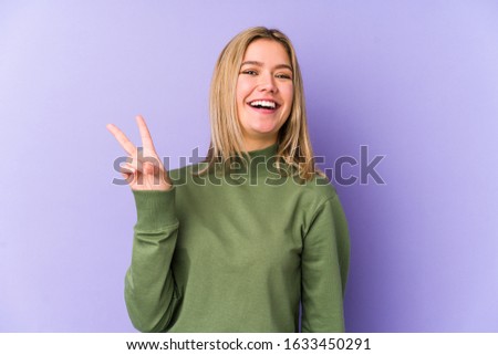 Young blonde caucasian woman isolated joyful and carefree showing a peace symbol with fingers.