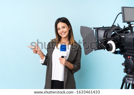 Reporter woman holding a microphone and reporting news over isolated blue background pointing finger to the side Royalty-Free Stock Photo #1633461433