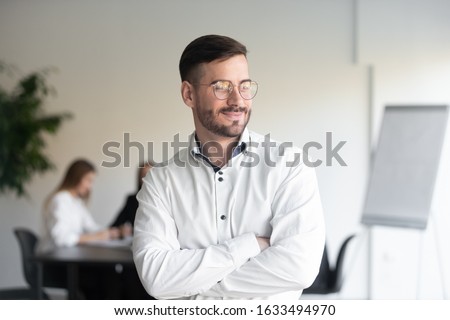 Smiling handsome businessman stands with arms crossed looks away feels satisfied proud about successful project work done, representative of confident manager company member, corporate leader concept