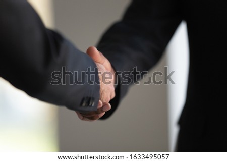 Concept close up image elegant African and Caucasian businessman in formal suits standing indoors shake hands as symbol of racial equality, business relations, boss and client, employer and employee