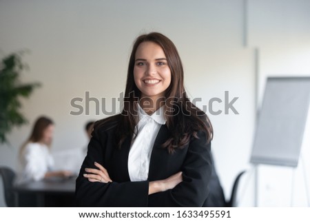 Head shot portrait of smiling businesswoman in elegant formal suit stands with arms crossed pose for picture at workplace, representative of young skilled professional, empowerment, leadership concept