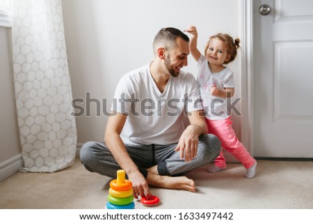 Young Caucasian father playing with child girl. Male man parent entertains toddler daughter sitting at home. Authentic lifestyle candid moment. Happy dad family day life concept. 