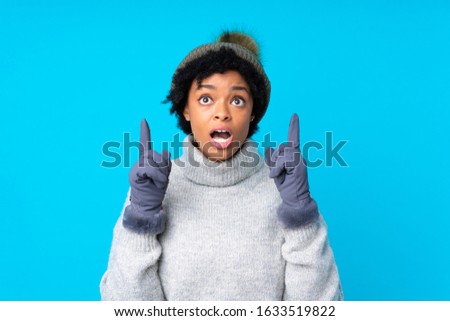 African american woman with winter hat over isolated blue background pointing with the index finger a great idea