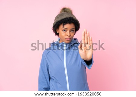African american woman with winter hat over isolated pink background making stop gesture with her hand