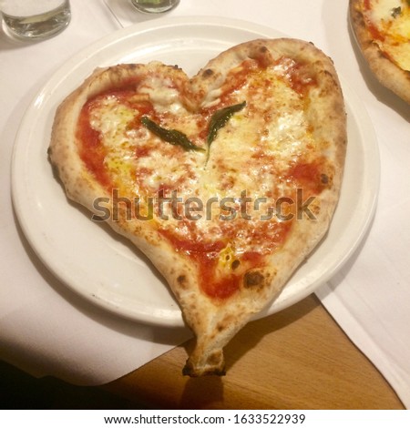 Pizza Margarita in the shape of a heart on a white plate and tablecloth in a South Tyrol restaurant 