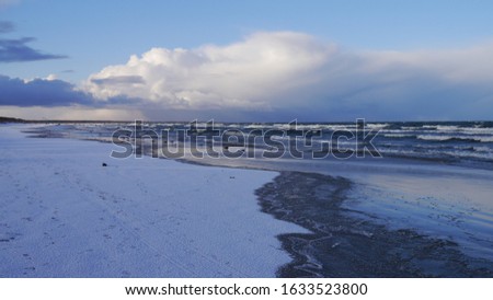 
Winter sea panorama. Snowy beach, waves at sea. Dark clouds in the sky.