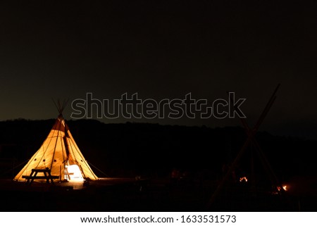 Night photo of the camping site in Japan. Yellow tent with light inside in the darkness. Stars in the sky.