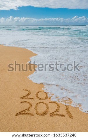 2020 2021 written in the sand with a wave erasing 2020- New Year’s concept