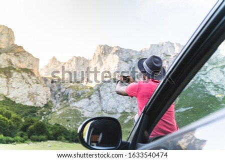 Young Man Relaxing on his Car While Enjoy the Nature. Man Sitting on the Car Bonnet Taking Picture to the Mountain. Latin American Guy Parked in a Natural Park and Relaxing on his Car. Travel Concept.