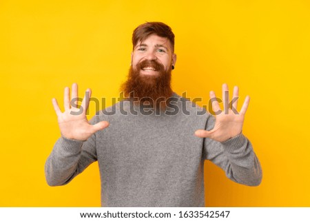 Redhead man with long beard over isolated yellow background counting ten with fingers