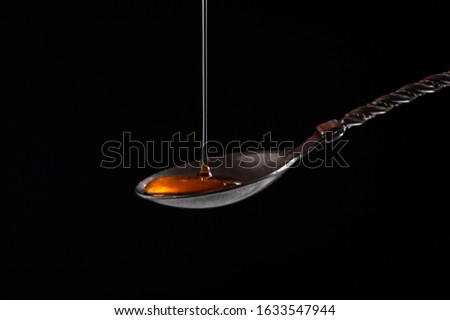  honey from above pours into a vintage silver spoon and fills it on a black background close-up