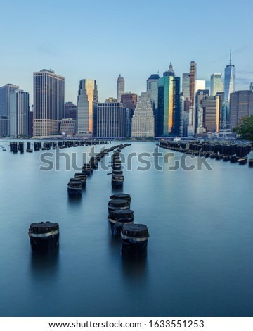 Lower Manhattan Skyline from Brooklyn Bridge Park Old Pier 1 with Pylons in the East River during Sunrise. The symmetrical curve leads the eye straight up to the impressive array of building