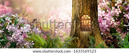 Enchanted fairy tale forest with magical shining window in hollow of fantasy pine tree elf house, blooming fabulous giant pink sakura cherry flower garden, building in wood in fairytale morning light Royalty-Free Stock Photo #1633569523
