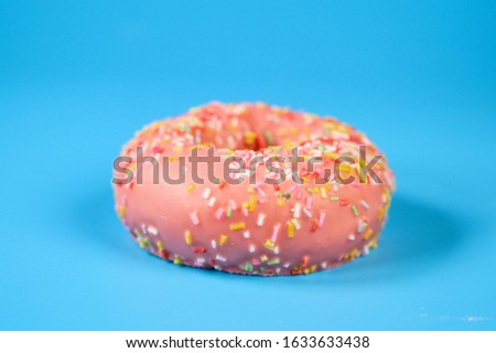 Pink iced donut on blue background. Sweet dessert top view .