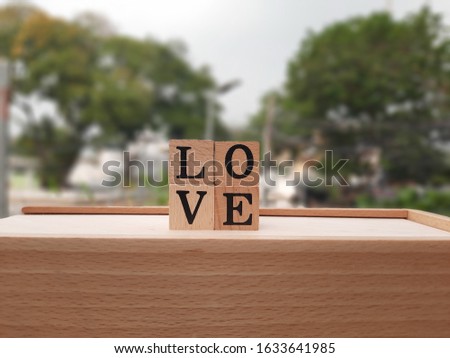 The image of four square wooden blocks with four letters L, O, V and E isolated on a wooden tray, shot with blurred background for decorative design and Valentine's Day.