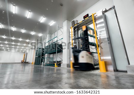 Worker Stand-on stacker truck used to lift and move the ready meals goods stock in cold room or freezer room. Royalty-Free Stock Photo #1633642321