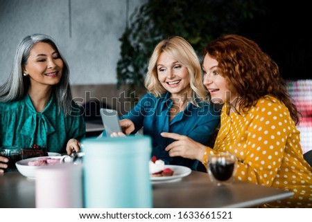 Cheerful women watching funny video on smartphone while sitting at cafe table stock photo
