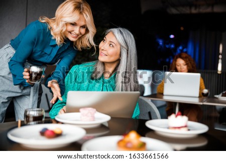 Smiling women sitting at the table with notebook while her female friend holding cup of tea stock photo