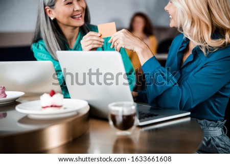 Close up of joyful ladies with plastic bank card in their hands sitting at the table in cafe stock photo