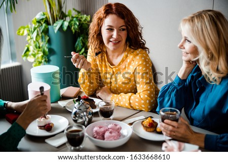 Cheerful female friends enjoying desserts and hot drinks in coffee house stock photo