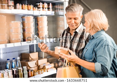 Waist up of smiling mature couple holding products in the store stock photo
