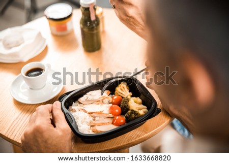Cropped photo of male eating food from box while sitting at the table stock photo