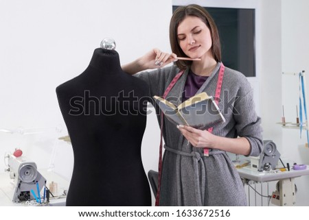 Brunette seamstress measuring black dummy in workshop, tailor studio work