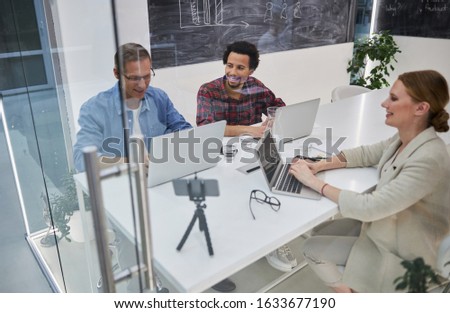 Friendly team. Smiling lady and two men sitting at the table and using laptops stock photo